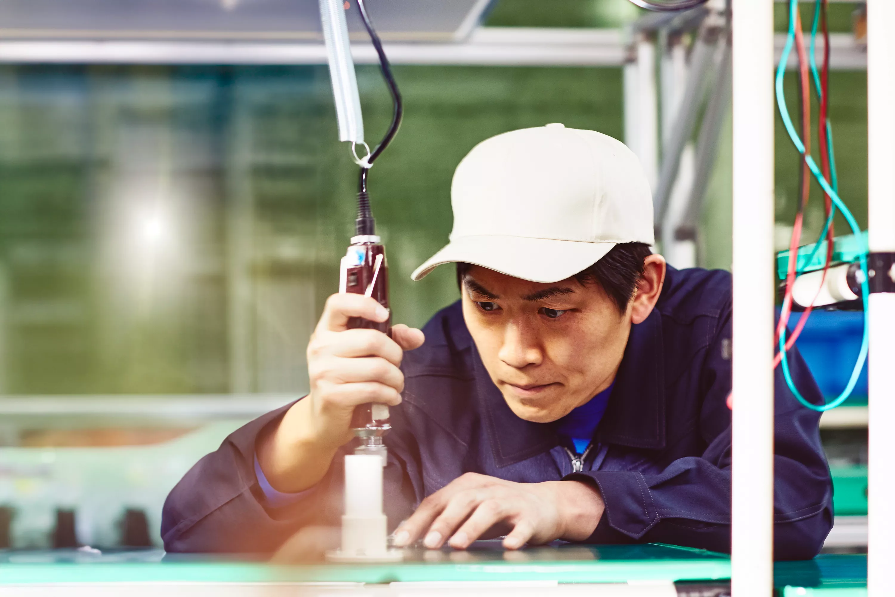 Mann mit weißer Kappe und blauem Overall, der mit Werkzeugen in einer Produktionsstätte arbeitet