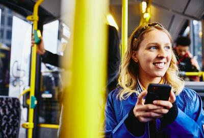 Lächelnde Frau mit Mobiltelefon im Bus